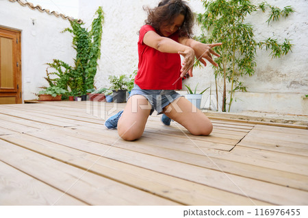 Young woman in casual clothing dancing expressively on a wooden deck outdoors 116976455