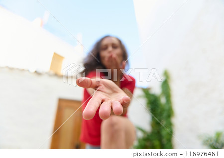 Woman blowing a kiss with an outstretched hand in a courtyard during daytime 116976461