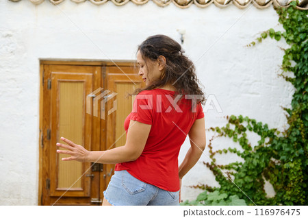 Woman in red shirt dancing in front of wooden door and ivy-covered wall 116976475