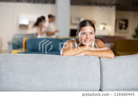 Woman choosing new sofa in furniture salon, testing softness of cushions and examining quality of upholstery Woman choosing new sofa in furniture salon, testing softness of cushions and examining quality of upholstery 116980445