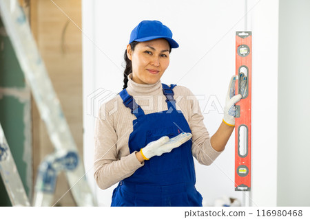 Woman builder using building level measures the vertical of wall 116980468