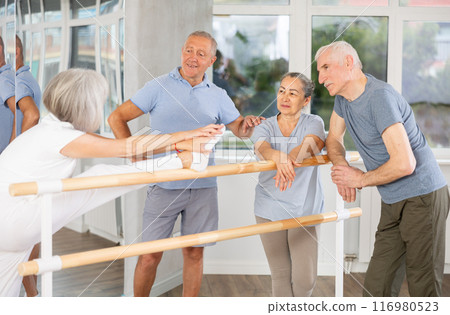Active old attendees of ballet courses communicating cheerfully at ballet-barre 116980523