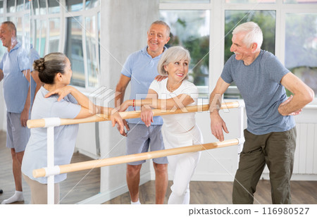 Active old attendees of ballet courses communicating cheerfully at ballet-barre 116980527