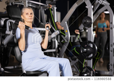 Focused mature female athlete using overhead press machine in gym Focused mature female athlete using overhead press machine in gym 116980588