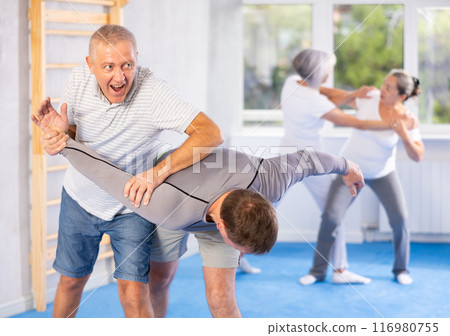 Self-defense lesson - mature man learns how to do painful hold with trainer in gym 116980755