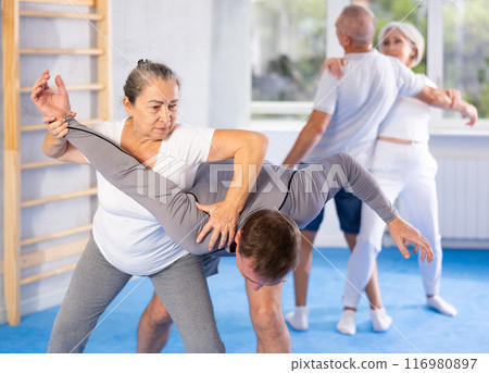 Mature woman learns how to do painful hold with trainer in gym. Self-defense lesson 116980897