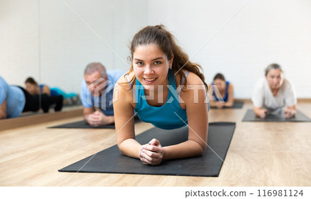 People of different ages in sportswear performing plank exercise during group Pilates workout in fitness studio 116981124