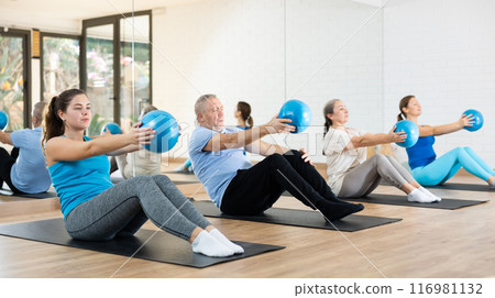 Group of young elderly people in sportswear exercising Pilates with mini balls while lying on mats in rehabilitation center 116981132