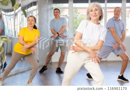 Elderly woman practicing Tai Chi with group in training room 116981170