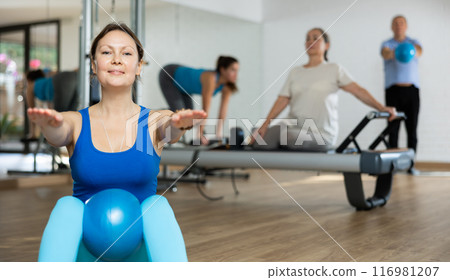 People of different ages pressing core and clutching mini Pilates balls between legs during Pilates training together People of different ages pressing core and clutching mini Pilates balls between legs during Pilates training together 116981207