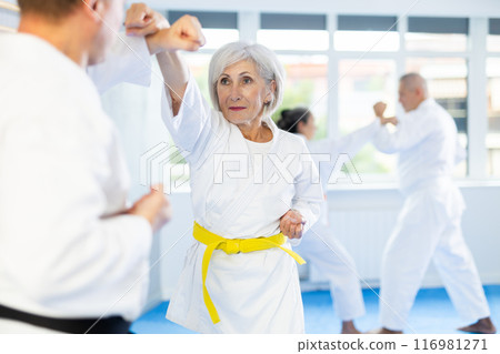 Old woman attendee of karate classes fighting with her opponent in sports hall 116981271