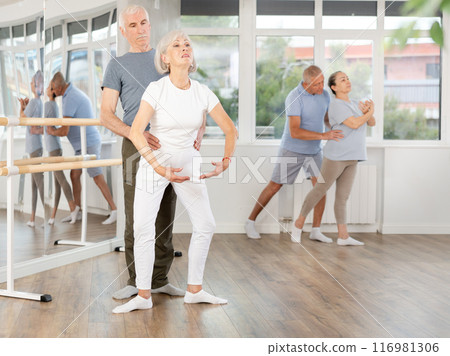 Mature woman practicing plie position in pair with man in dance studio Mature woman practicing plie position in pair with man in dance studio 116981306