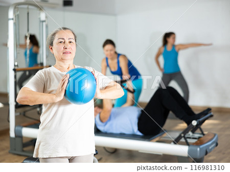 Aged woman practicing pilates with ball in fitness hall Aged woman practicing pilates with ball in fitness hall 116981310