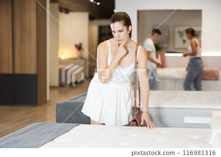 Young woman choosing convenient mattress in furniture shop 116981316