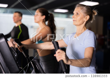 Sporty senior woman exercising on elliptical trainer in gym 116981333