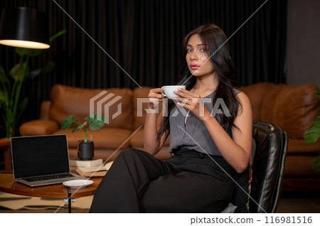 A gorgeous Asian businesswoman is resting in her office, sipping coffee, and looking at the camera. A gorgeous Asian businesswoman is resting in her office, sipping coffee, and looking at the camera. 116981516