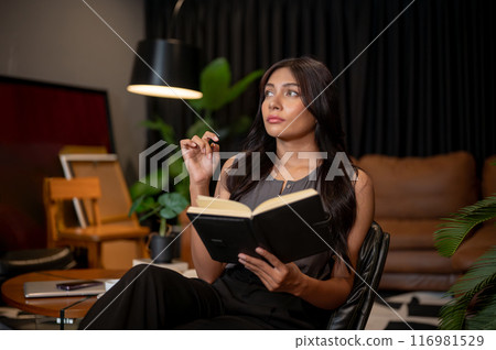 A thoughtful Asian businesswoman is sitting in a chair in a room with a notebook in her hand. A thoughtful Asian businesswoman is sitting in a chair in a room with a notebook in her hand. 116981529