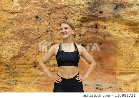 Smiling slim fit blonde woman stands near rock outdoors 116981721