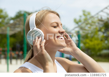 Smiling young woman with headphones on sports field, close up 116981725