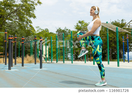 Slim fit woman with headphones doing exercises on sports field, space for text Slim fit woman with headphones doing exercises on sports field, space for text 116981726