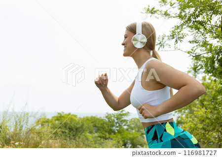Strong athletic woman in sportswear with headphones running outdoors, space for text 116981727