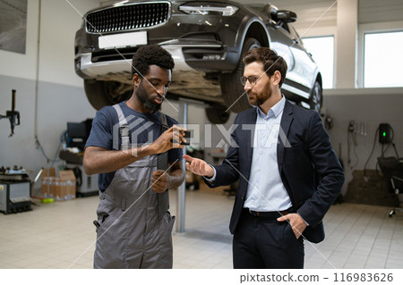 Mechanic discussing vehicle repair details with customer in auto workshop Mechanic discussing vehicle repair details with customer in auto workshop 116983626