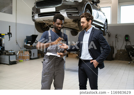 Mechanic handing car keys to businessman in auto repair shop Mechanic handing car keys to businessman in auto repair shop 116983629
