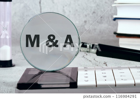M and A Mergers and Acquisitions, word concept. M and A appeared through a magnifying glass on a gray wall. Photos in black and white 116984291