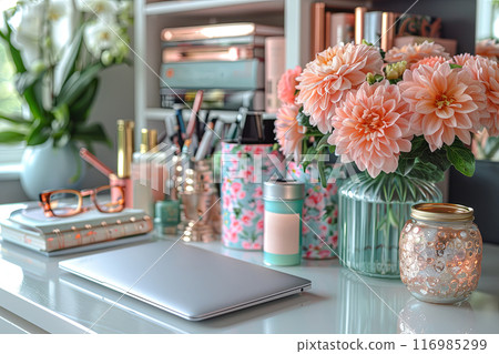Desk with a laptop, a vase of flowers, and a few books. The desk is organized and has a pleasant, inviting atmosphere 116985299