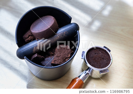 Compacted coffee ground in knock box with portafilter next to it. Coffee grounds are excellent natural and organic fertilizers. Compacted coffee ground in knock box with portafilter next to it. Coffee grounds are excellent natural and organic fertilizers. 116986795