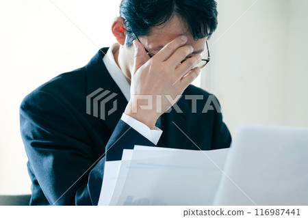 Businessman worried about looking at documents Businessman worried about looking at documents 116987441