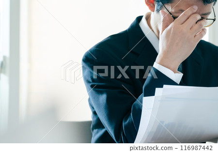 Businessman worried about looking at documents Businessman worried about looking at documents 116987442
