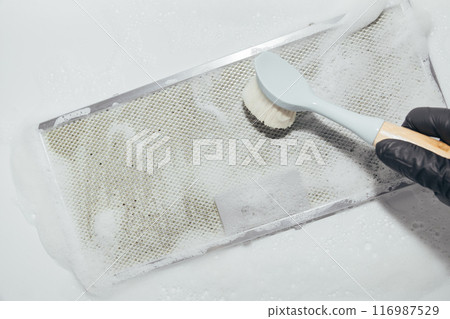Hand in black glove cleaning mesh filter of cooker hood with brush and foam, white background Hand in black glove cleaning mesh filter of cooker hood with brush and foam, white background 116987529