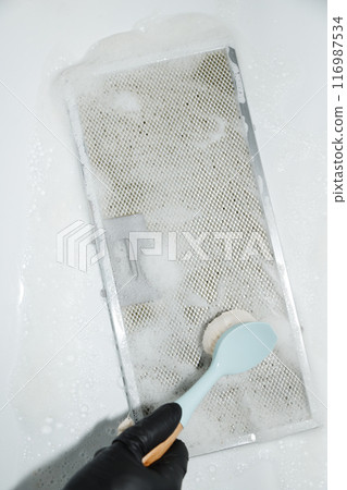 Hand in black glove cleaning mesh filter of cooker hood with brush and foam, white background Hand in black glove cleaning mesh filter of cooker hood with brush and foam, white background 116987534