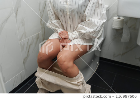 close up woman sitting on toilet bowl and holding her painful Stomach in bathroom 116987606