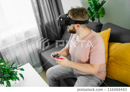 Man playing video games in living room sitting on sofa. 116988483