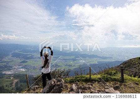 A young woman wearing a hat climbing Mt. Ibuki, stretching her arms and looking at the view A young woman wearing a hat climbing Mt. Ibuki, stretching her arms and looking at the view 116988611