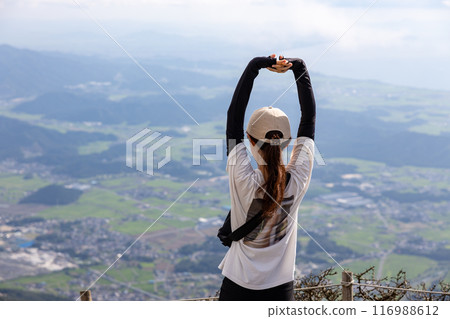 一位戴著帽子的年輕女子爬上伊吹山，伸出雙手，眺望風景。 116988612