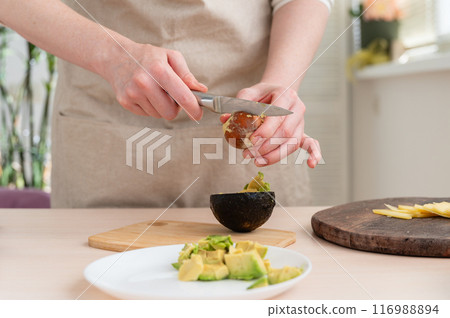 Woman cutting fresh avocado in kitchen. Close-up. Woman cutting fresh avocado in kitchen. Close-up. 116988894