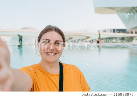Young traveling woman taking selfie outdoors. Concept of travel, tourism and vacation in city. Ciudad de las Artes y las Ciencias de Valencia.Valencia City of Arts and Sciences. High quality photo 116988975