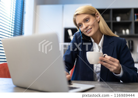 Woman professional manager using laptop while having phone conversation with cup of coffee in office 116989444