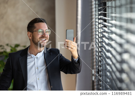 Businessman in business suit uses telephone near window for online video call Businessman in business suit uses telephone near window for online video call 116989481