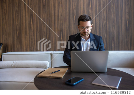 Successful man entrepreneur in formal business suite sitting on sofa with laptop in office interior 116989512