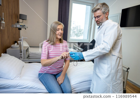 Gray-haired male doctor examining a patient in the admissions 116989544