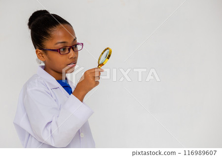 Side view of African American kid wearing white lab coat with magnifier isolated on white background Side view of African American kid wearing white lab coat with magnifier isolated on white background 116989607