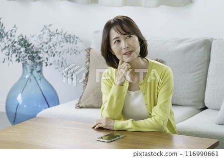 一位中年婦女坐在客廳裡,歪著頭 一位中年婦女坐在客廳裡,歪著頭 116990661