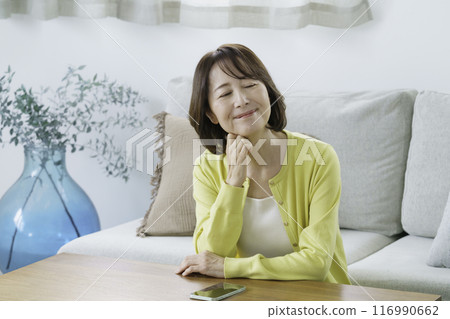 A middle-aged woman smiling with her eyes closed sitting in the living room A middle-aged woman smiling with her eyes closed sitting in the living room 116990662
