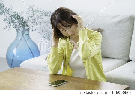 A middle-aged woman sitting in the living room and holding her head A middle-aged woman sitting in the living room and holding her head 116990665