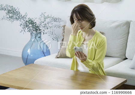A middle-aged woman sitting in the living room, covering her eyes 116990666