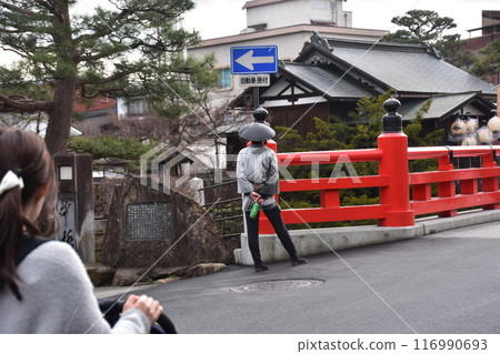 Spring in Japan: Old streetscape of Takayama City, Gifu Prefecture: A rickshaw driver waiting for a customer at Nakabashi Bridge in the center of the city, a female tourist passing by 116990693